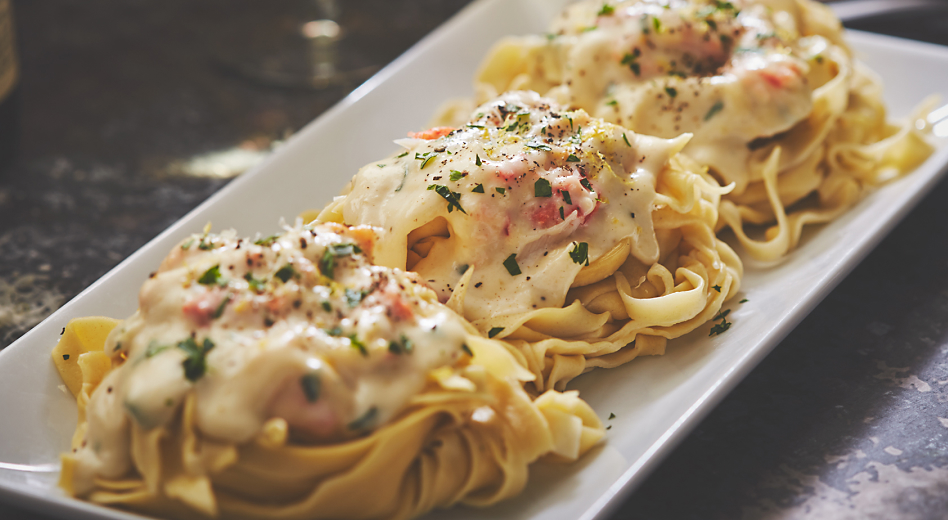 Three nests of fettuccine pasta topped with melted cheese on a plate