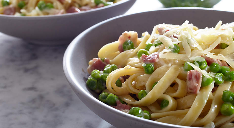 Fettuccine with cream sauce topped with peas, bacon and grated cheese