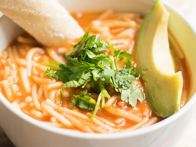 Bowl of sopa de fideo topped with fresh herbs, avocado slices and a breadstick