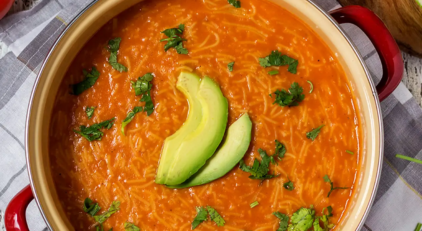 Pot of sopa de fideo topped with fresh herbs and avocado slices