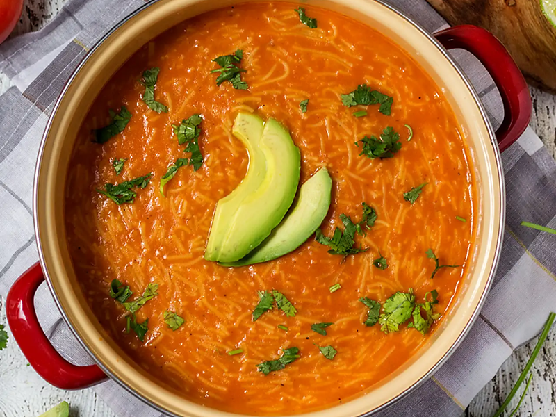 Pot of sopa de fideo topped with fresh herbs and avocado slices
