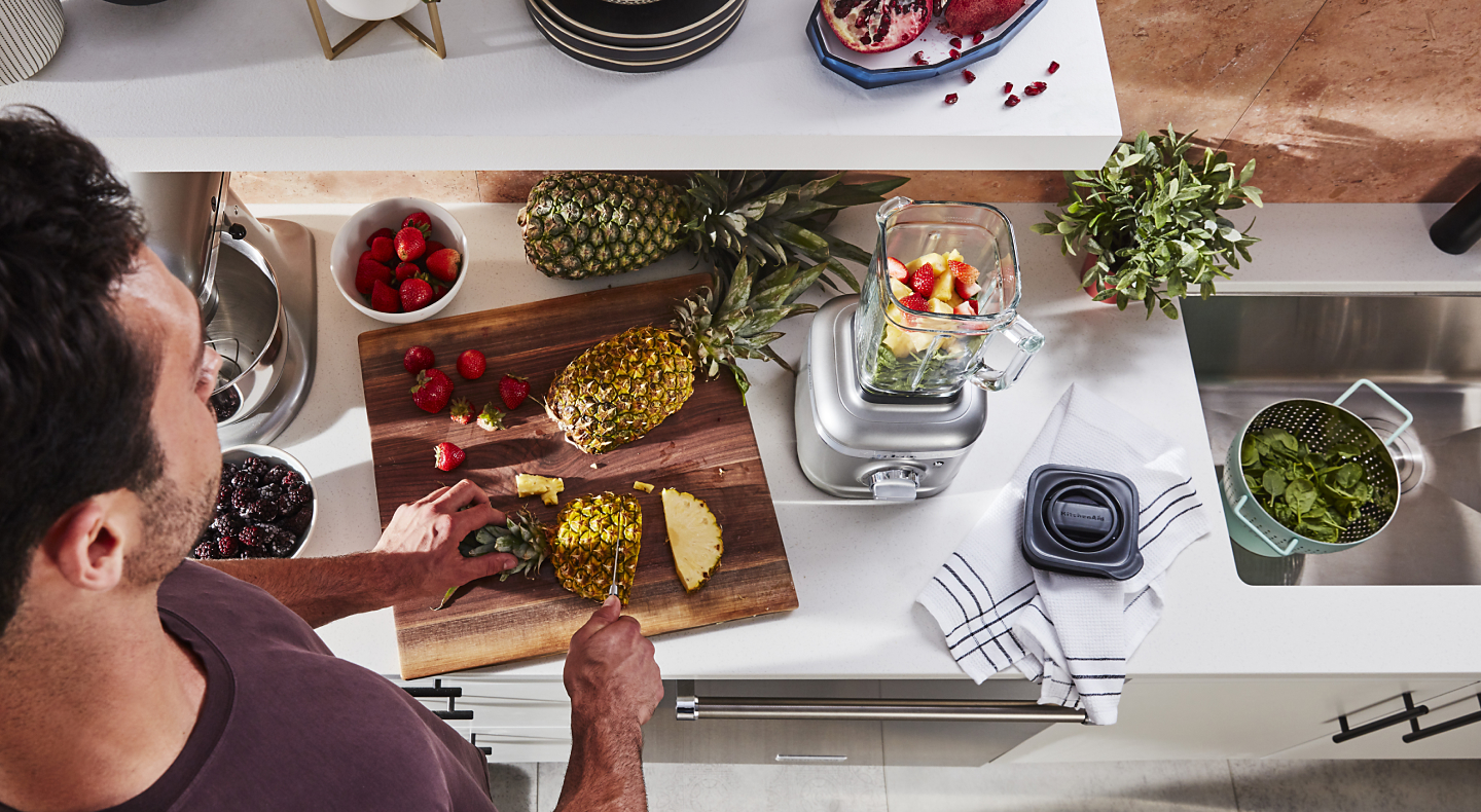 Person cutting pineapple next to KitchenAid® blender with fruit in it