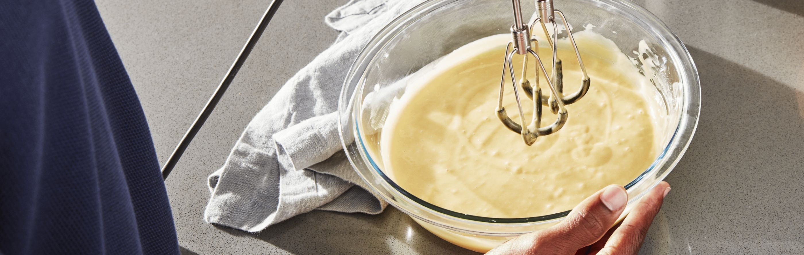 Person using hand mixer to mix white queso in glass bowl
