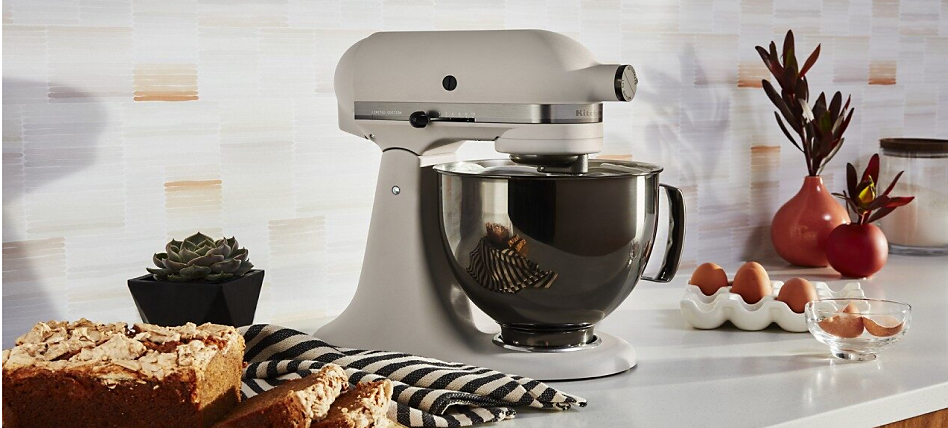 A white KitchenAid® stand mixer beside sliced loaf cake and eggs