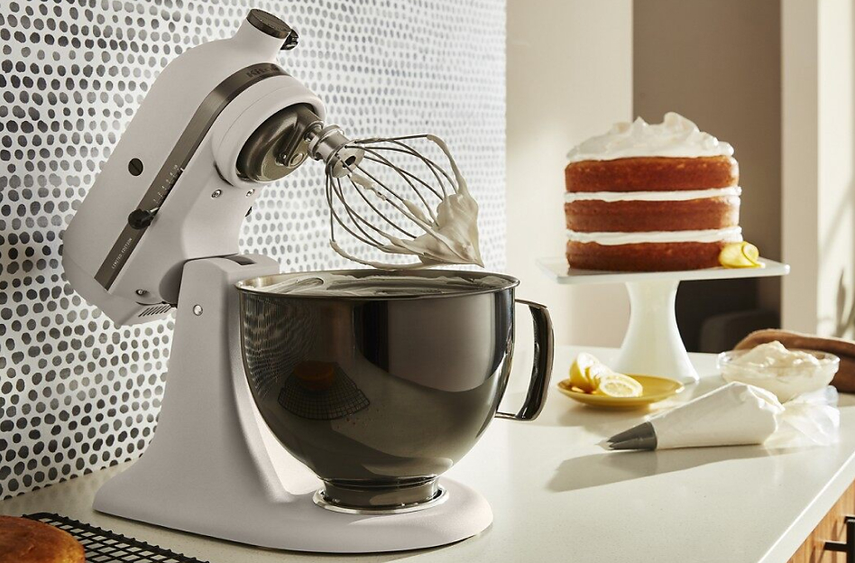 A KitchenAid® stand mixer with whisk attachment and a vanilla frosted cake 