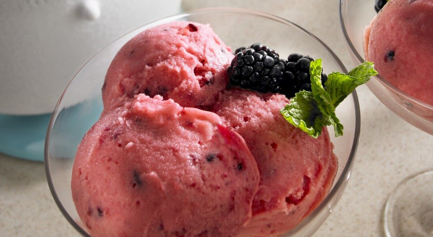 Strawberry ice cream in a glass dish, topped with berries and garnish.