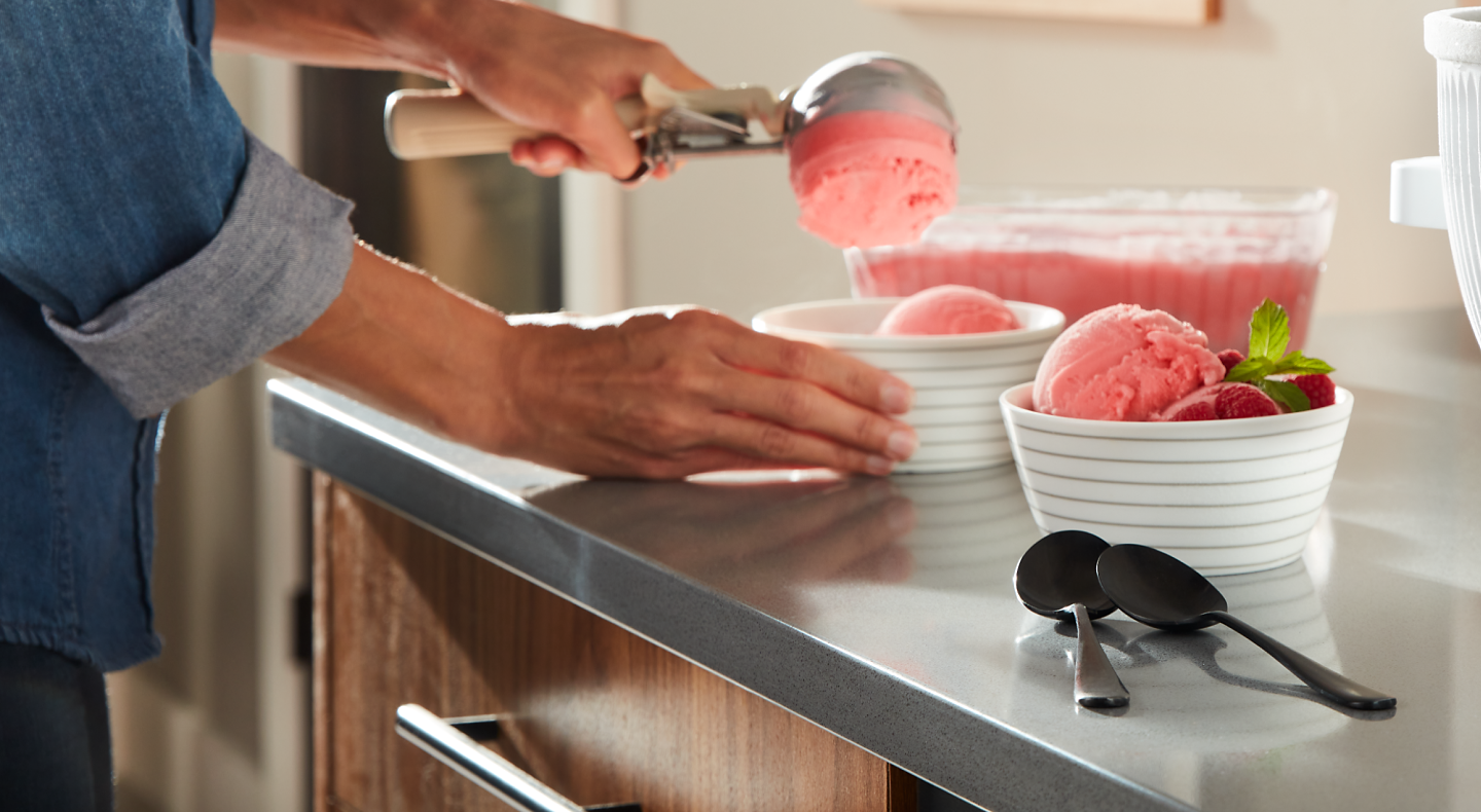 A person scooping strawberry ice cream into dishes.