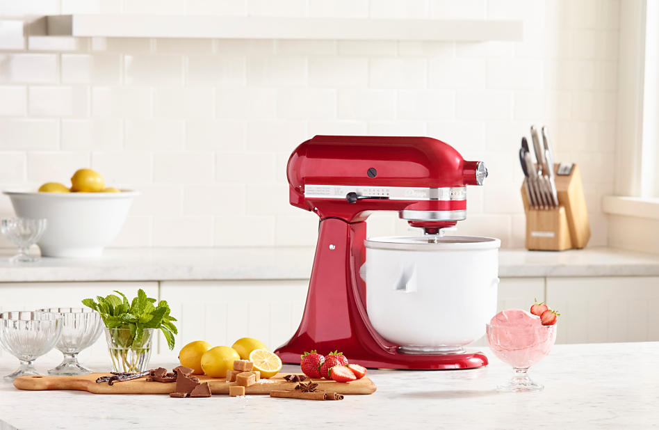 Red stand mixer with ice cream maker attachment on counter with ingredients