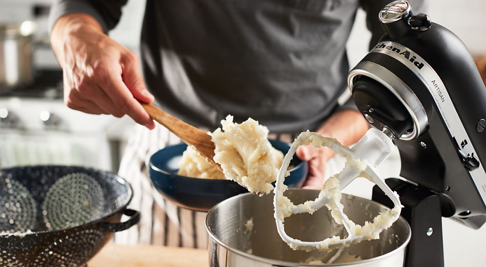Man scooping mashed potatoes out of a stand mixer with paddle