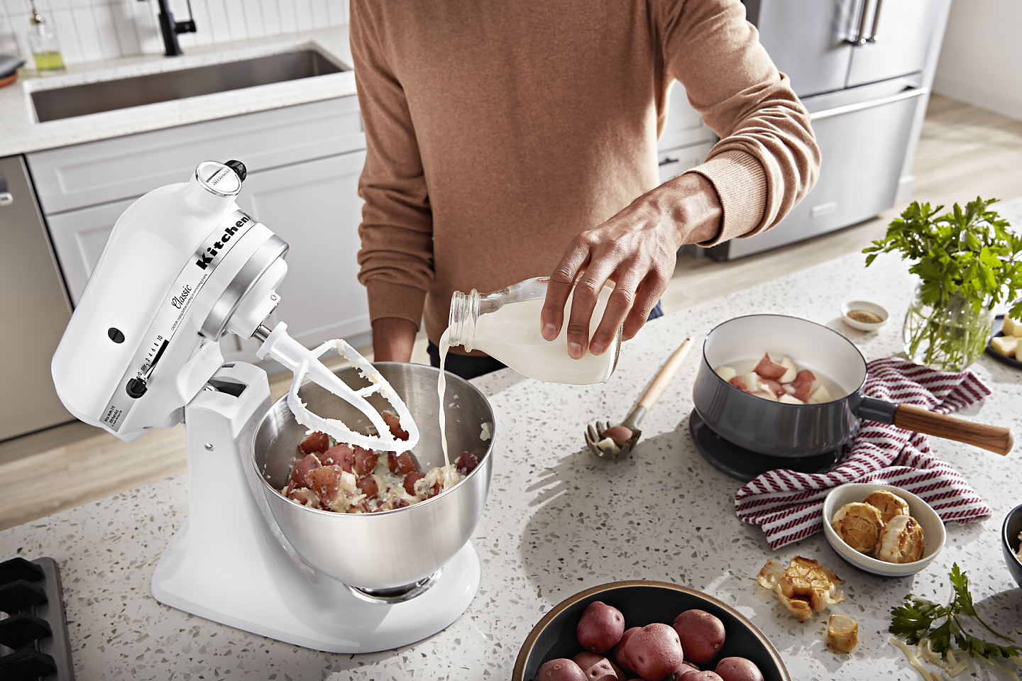 Man pouring milk into a stand mixer bowl of mashed potatoes