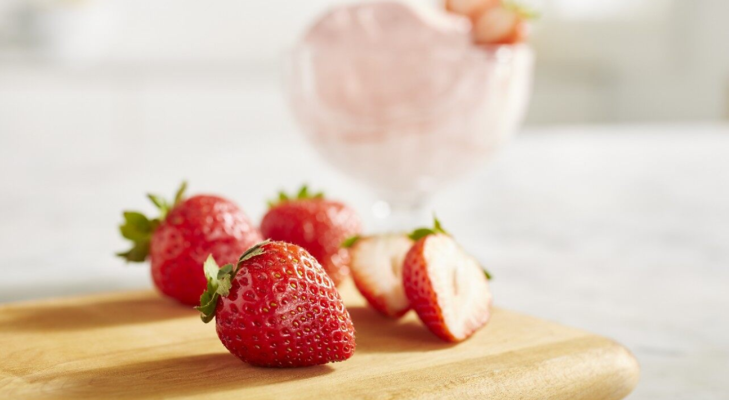 A closeup of fresh strawberries next to a dish of strawberry nice cream