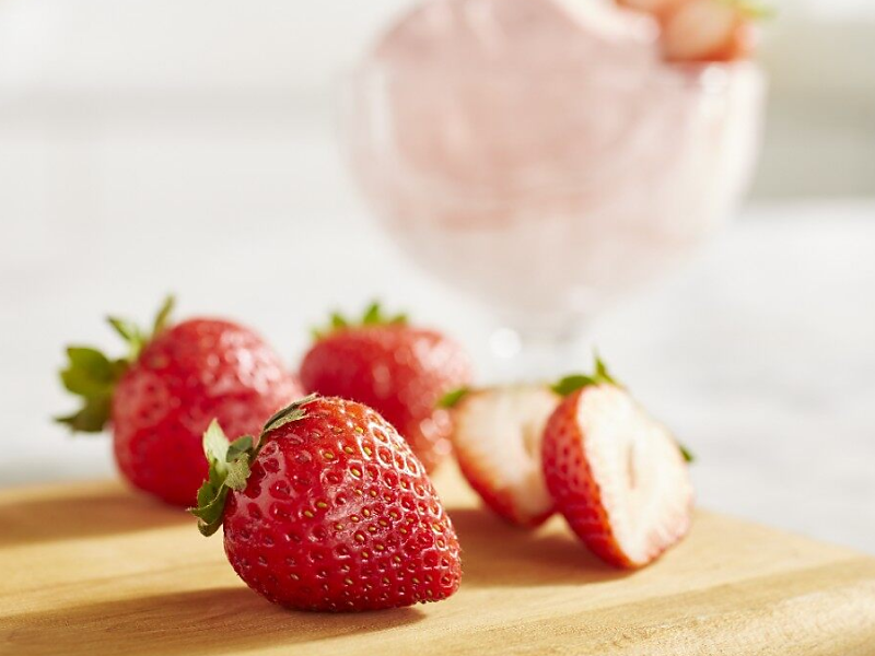 A closeup of fresh strawberries next to a dish of strawberry nice cream
