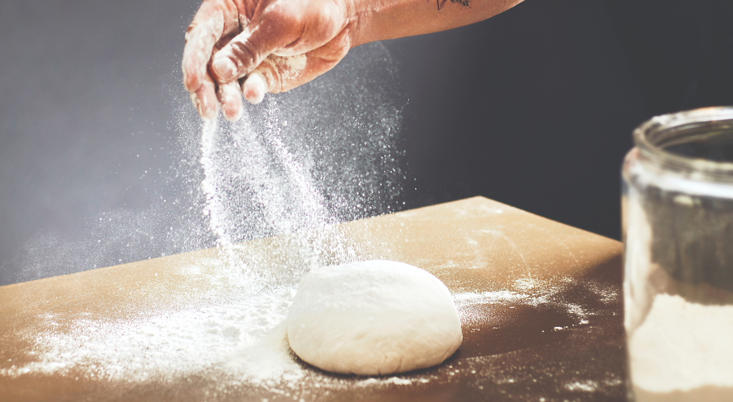 Person sprinkling flour over a ball of dough