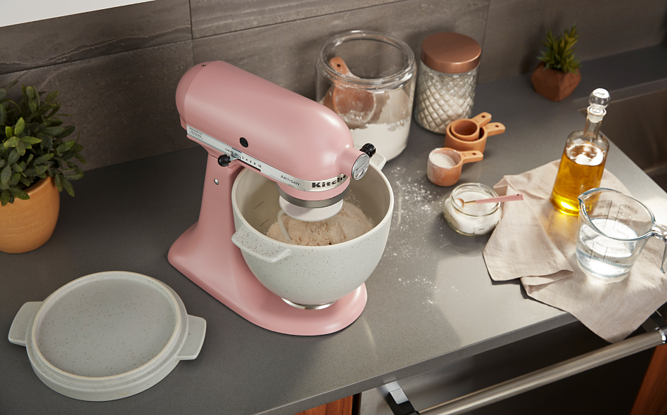 Top view of pink KitchenAid® Stand Mixer filled with bread dough standing on counter surrounded by other baking ingredients