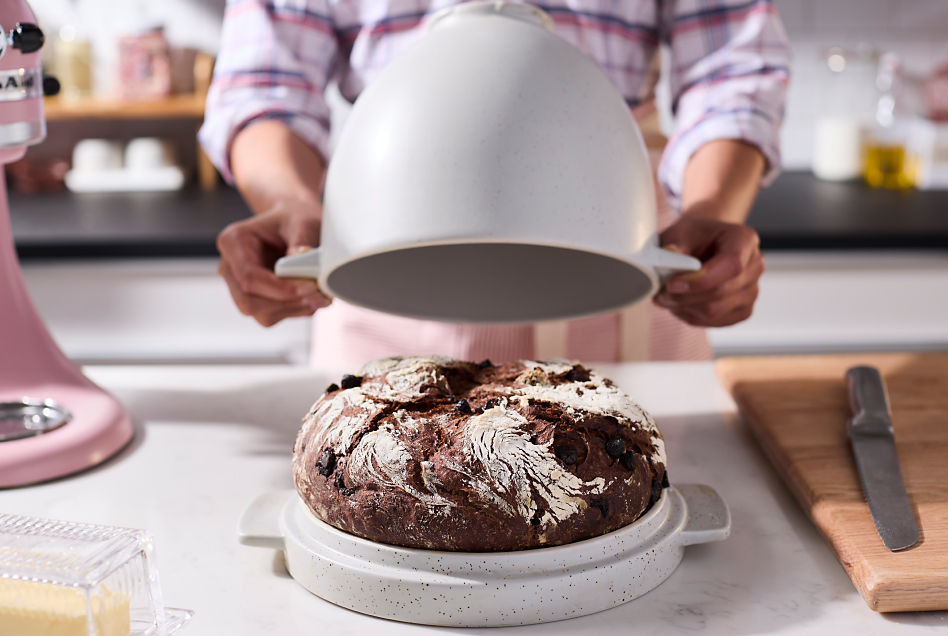 Maker uncovering top of bread bowl to reveal baked rye bread loaf