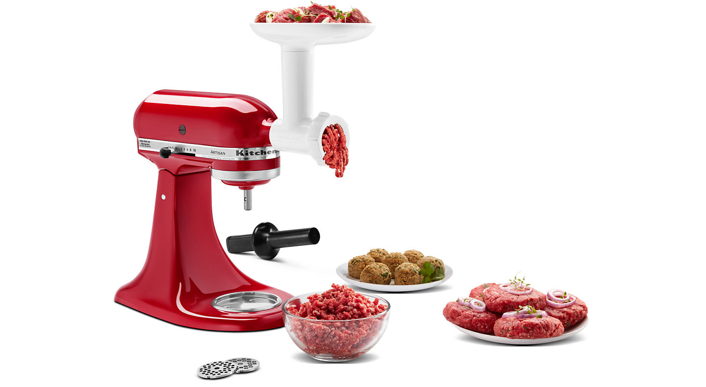 KitchenAid® stand mixer and meat grinder attachment grinding meat into bowl with plate of short rib patties and meatballs