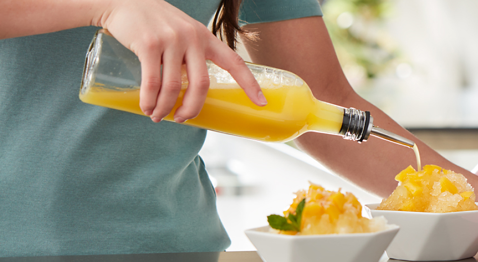 Syrup being poured on an ice dessert surrounded by mango and KitchenAid stand mixer.