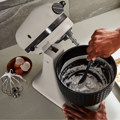A person removing cream from a white KitchenAid® stand mixer