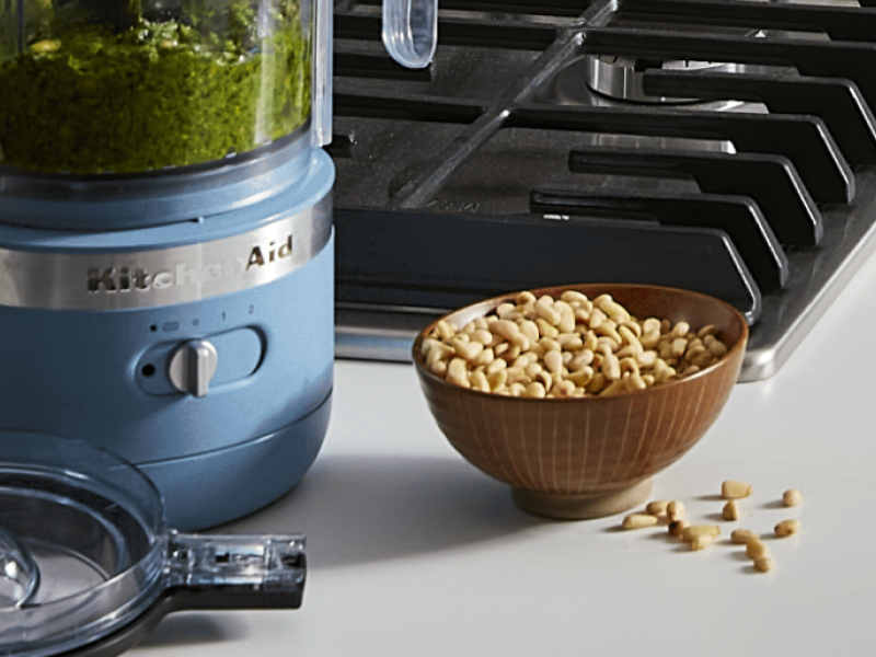 A KitchenAid® food processor with a bowl of nuts nearby.