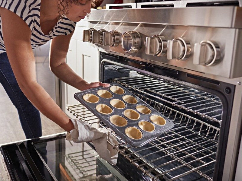 Person loading miniature pie shells in a muffin tin into the oven