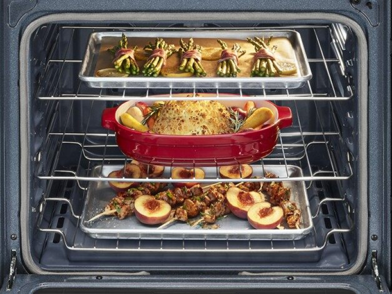 Open kitchen oven with roasting vegetables, fruits and meat on different racks