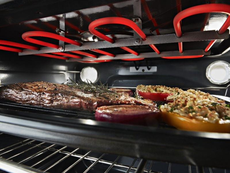 Close-up of roasting meat and vegetables beneath an oven heating element