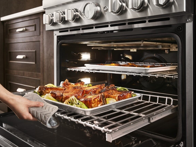 Person sliding out the bottom oven rack with a pan of food on top