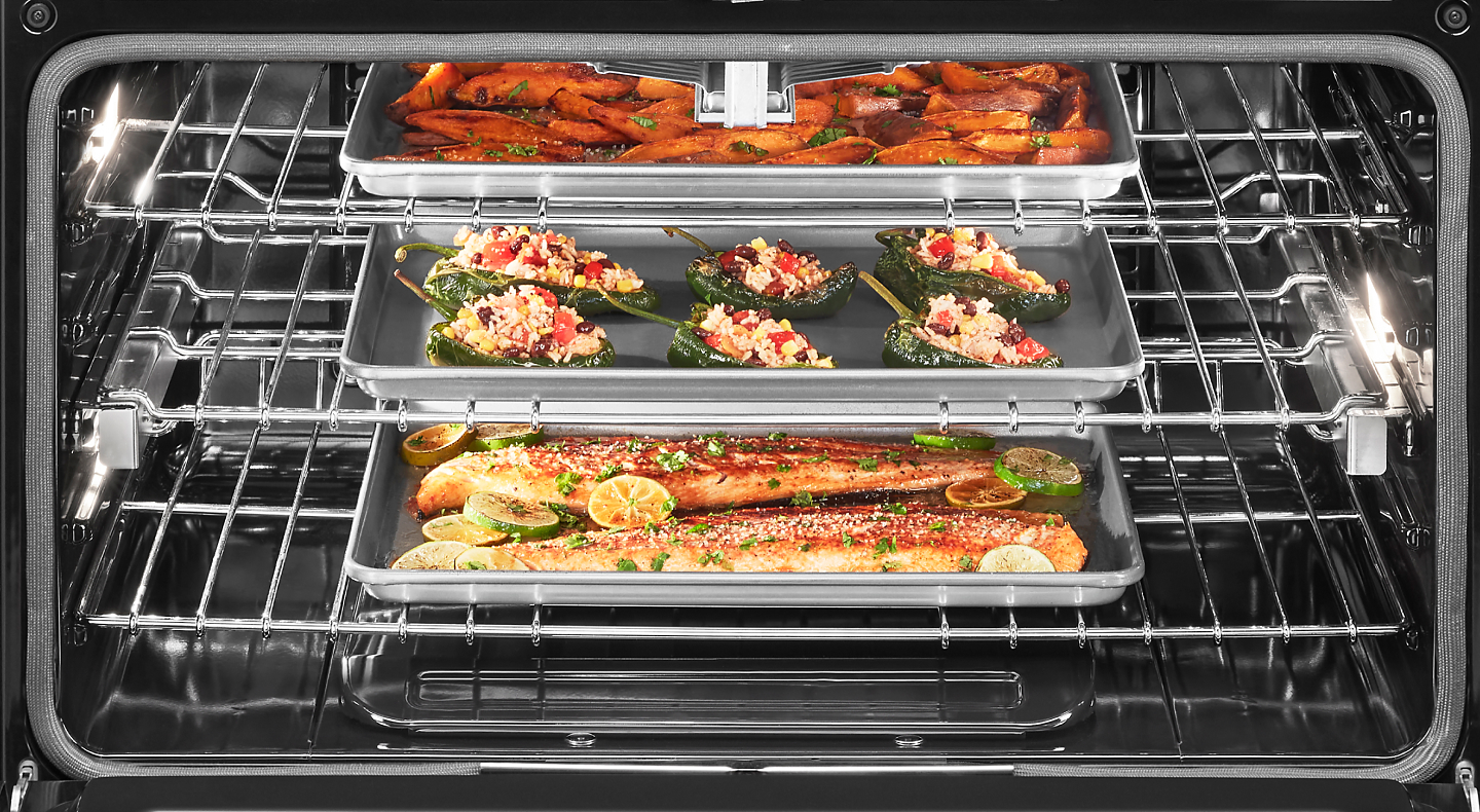 Open oven cavity with three pans roasting fish and vegetables inside