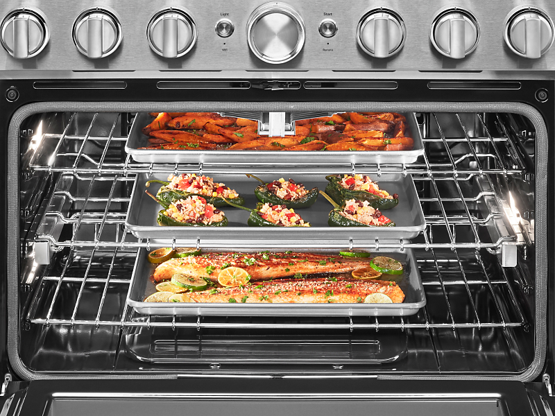 Open oven cavity with three pans roasting fish and vegetables inside