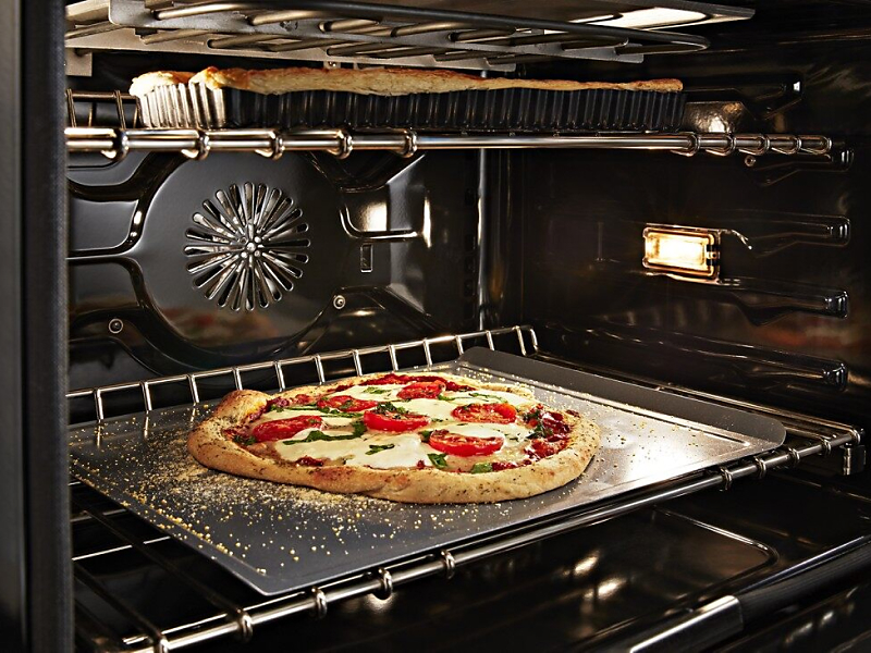 Artisan pizza baking in a convection oven with a dish baking on the rack above
