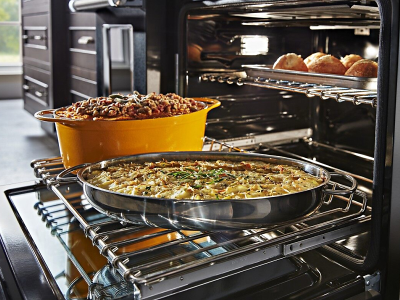 Casseroles sitting on top of an extended bottom oven rack with a dish cooking above