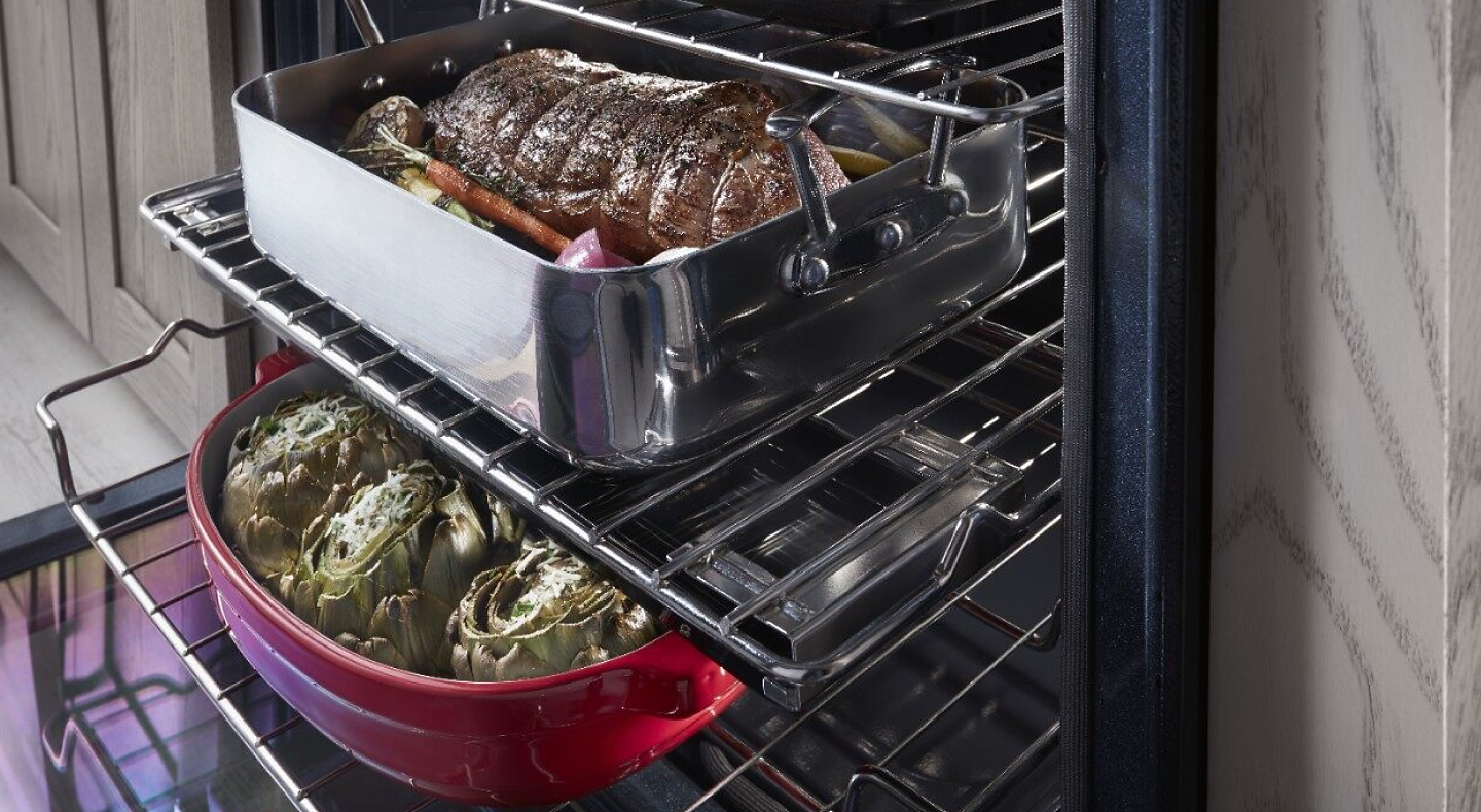Close-up of two large meat and vegetable dishes sitting on top of extended bottom and top oven racks