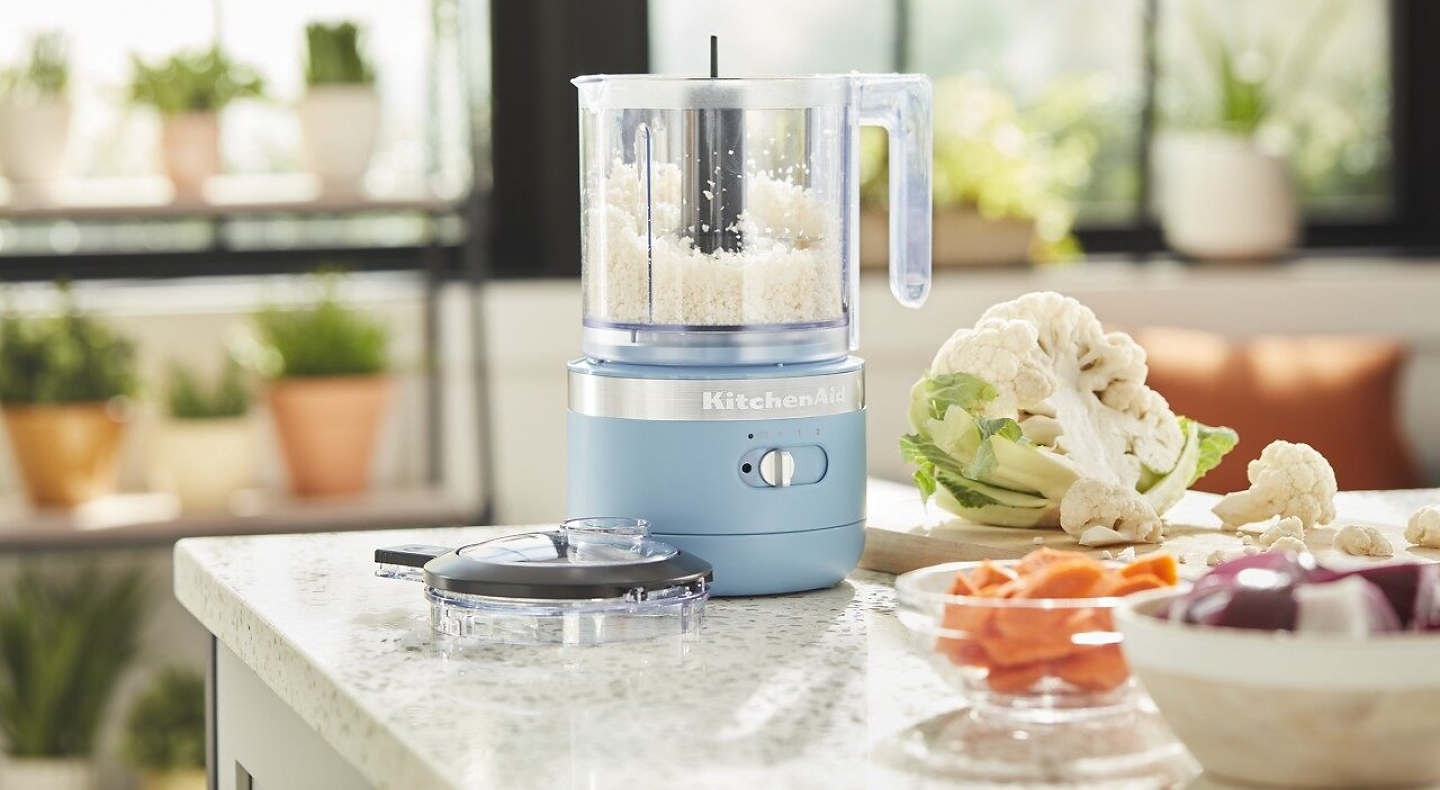 KitchenAid® food processor on a counter next to fresh vegetables in a modern kitchen. 