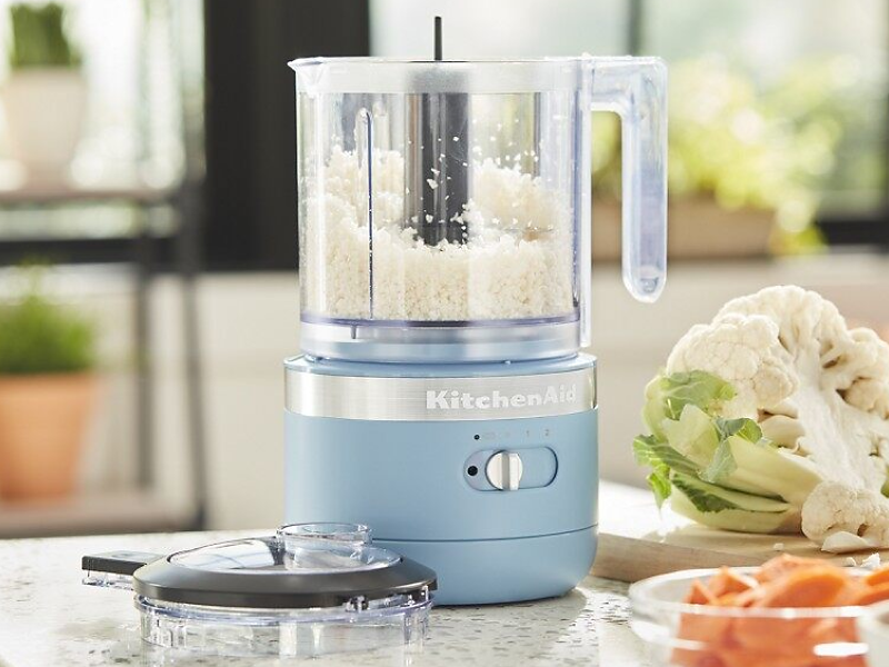 KitchenAid® food processor on a counter next to fresh vegetables in a modern kitchen. 
