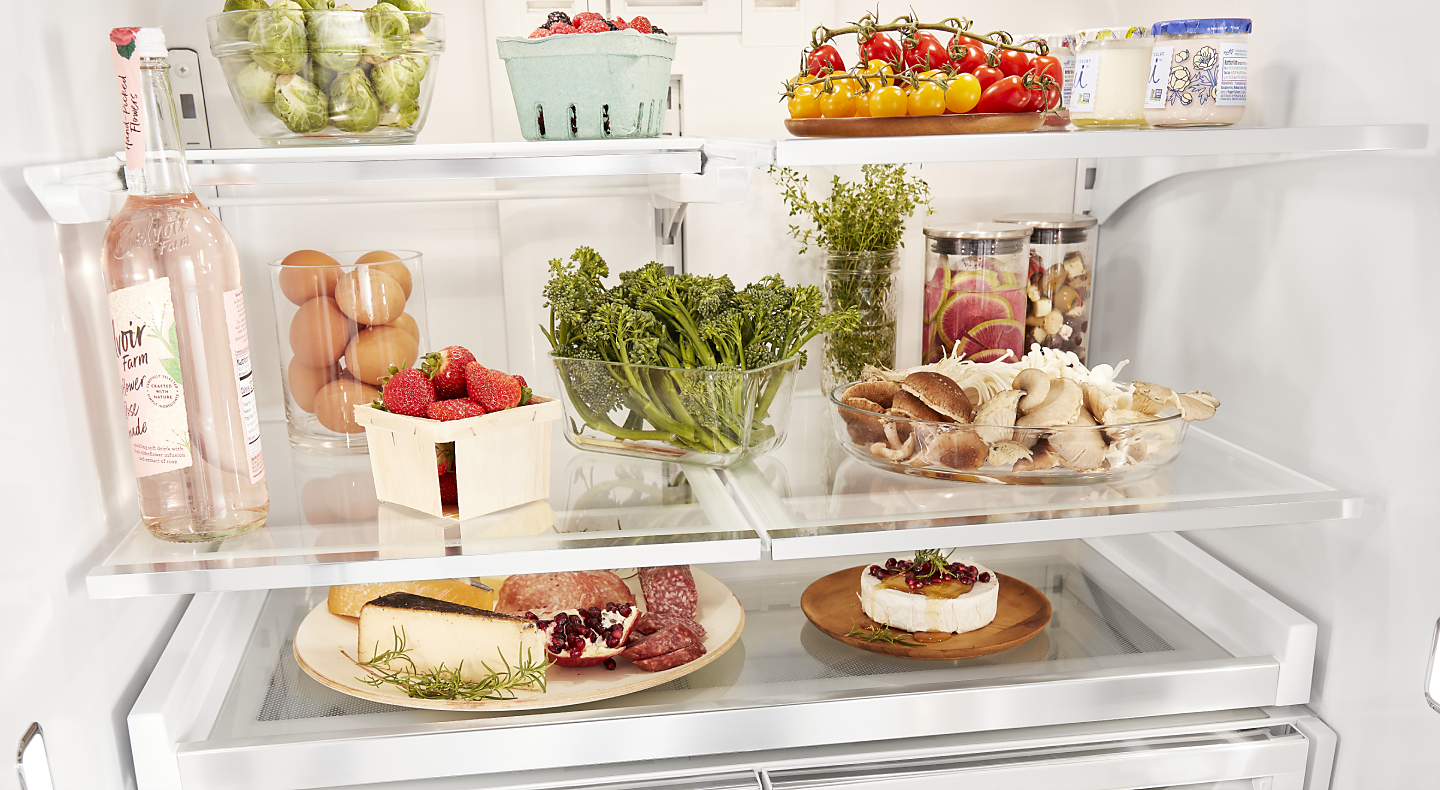 A charcuterie plate, herbs, fruits and vegetables organized on fridge shelves.