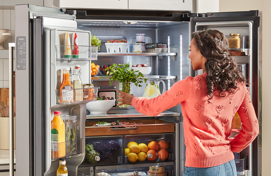 A woman placing a jar of herbs on a top refrigerator shelf.