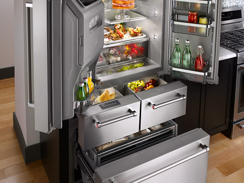 The doors and various compartments of a French door refrigerator open with groceries inside