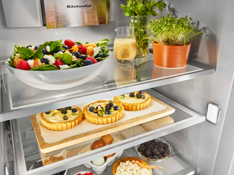 A salad, fruit desserts and several other dishes made from fresh ingredients inside an open French door refrigerator