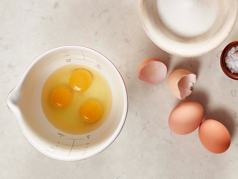 Three eggs in a bowl next to cracked egg shells