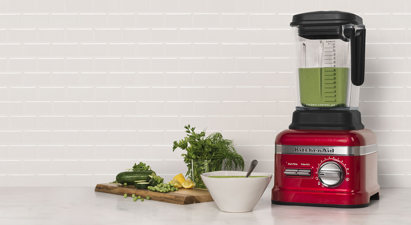 Red KitchenAid® blender next to various vegetables