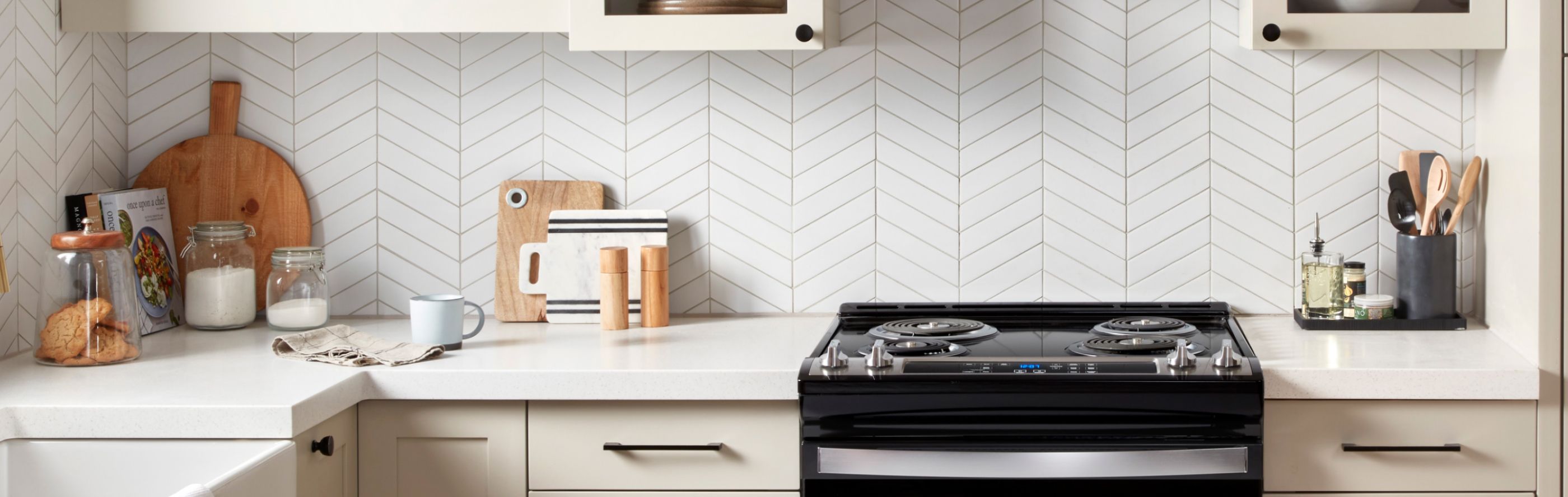Black electric stove between cream cabinetry in front of a white herringbone backsplash