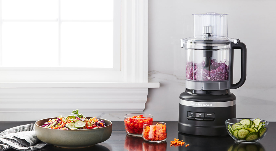 Salad topped with shredded carrots next to a black KitchenAid® food processor