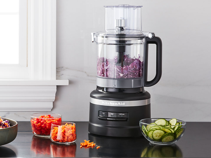 Salad topped with shredded carrots next to a black KitchenAid® food processor
