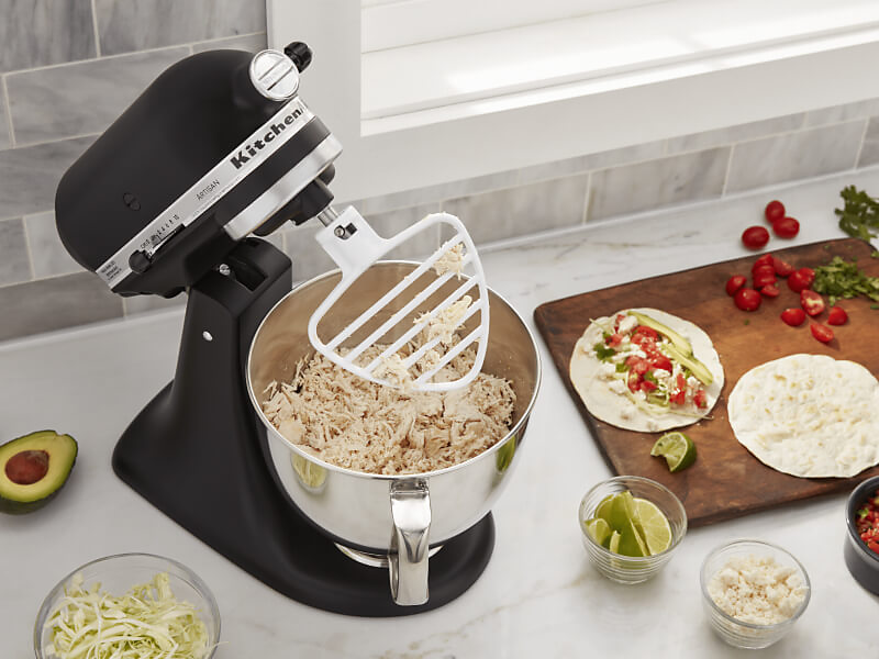 KitchenAid® stand mixer on a modern kitchen counter shredding cooked chicken.