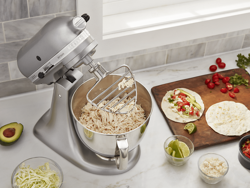 KitchenAid® stand mixer on a modern kitchen counter shredding cooked chicken.