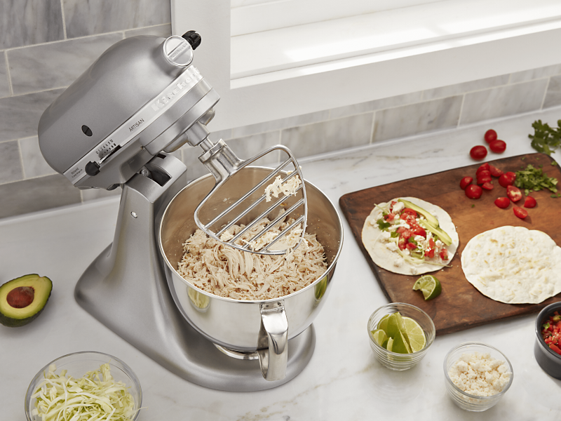 KitchenAid® stand mixer on a modern kitchen counter shredding cooked chicken. KitchenAid® stand mixer on a modern kitchen counter shredding cooked chicken.