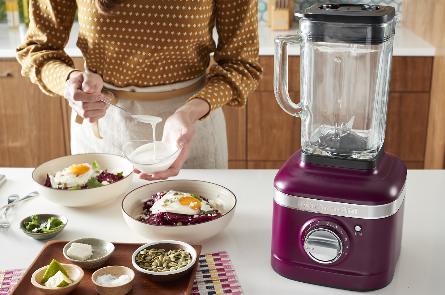 Woman preparing a meal next to a KitchenAid® blender. Woman preparing a meal next to a KitchenAid® blender.