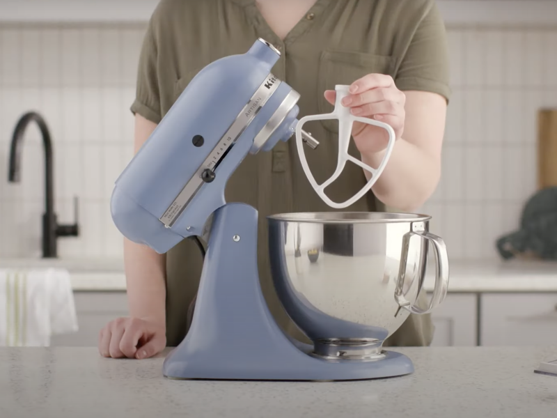 Woman holding a flat beater attachment next to a KitchenAid® stand mixer.