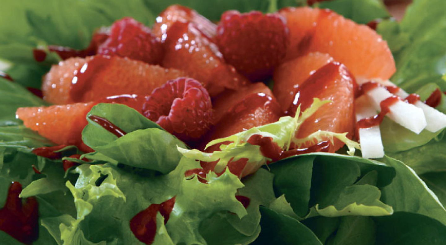 Close-up of raspberries and grapefruit topping shredded greens 