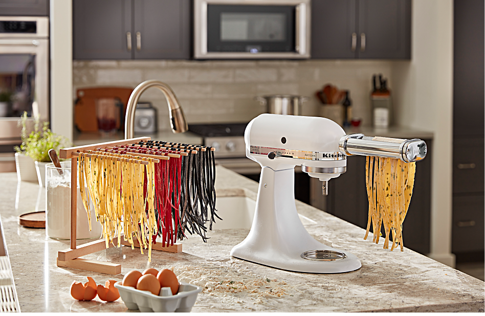 Three different colors of homemade spaghetti noodles drying beside a stand mixer